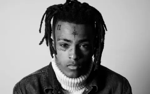 Czarno-białe zdjęcie rapera z tatuażami na twarzy, w golfie i kurtce dżinsowej. Wiele osób wspominało go, kiedy umarł xxxtentacion.
