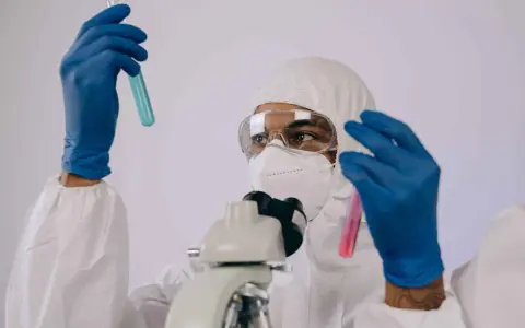 Badacz w kombinezonie i masce analizuje próbki w probówkach, przygotowując się do pracy w laboratorium chemicznym.