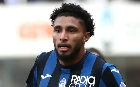 Primer plano de Éderson dos Santos, jugador de fútbol con pelo rizado y barba, vistiendo una camiseta a rayas azules y negras.