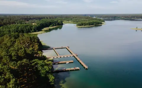 Drewniane pomosty na spokojnym jeziorze Wiartel, otoczonym gęstym lasem. Woda jest przejrzysta, a na pomostach stoją łódki i kajaki.