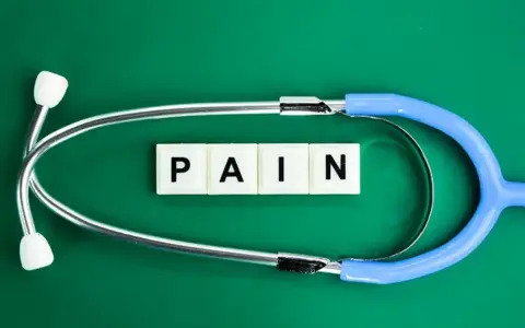 Stetoskop i kostki z literami "PAIN" symbolizują ból, który może być klasyfikowany według ICD-10.