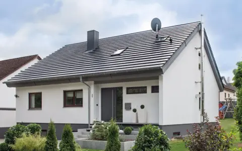 Nowoczesny dom z białymi ścianami i szarym dachem o kącie nachylenia dachu 30 stopni. Na dachu komin, anteny i okna dachowe.
