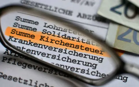 Lupe über Dokument mit hervorgehobener Kirchensteuer. Geld liegt daneben.