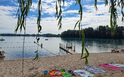Ein sonniger Tag am Lauterbourg See. Handtücher liegen am Sandstrand, Kinder planschen im Wasser.