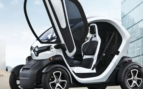 Biały, dwumiejscowy kei car z otwartymi drzwiami, zaparkowany przed nowoczesnym budynkiem.