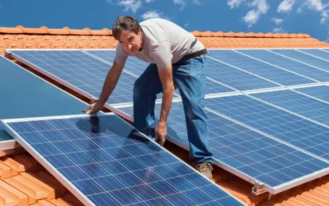 Instalator montuje panele fotowoltaiczne na dachu. Pokazuje, jak zamontować panele fotowoltaiczne, by czerpać energię ze słońca.
