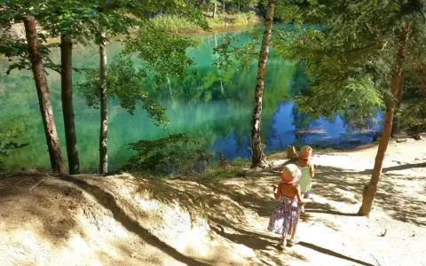 Dwie dziewczynki w słomkowych kapeluszach idą ścieżką nad turkusowe jezioro. Idealne miejsce, gdzie w góry z dziećmi latem.