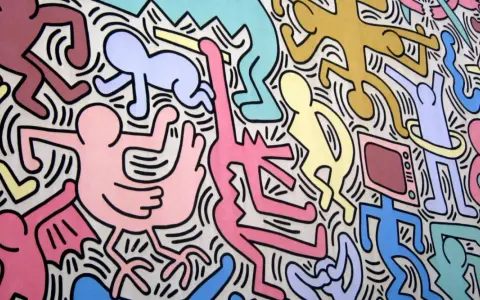 Une fresque colorée de Keith Haring, œuvre la plus connue, avec des figures stylisées dansant et interagissant, un chien jaune, un bébé et une télévision.