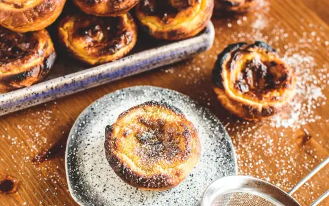 Leckeres Pastel de Nata Rezept: goldbraune Törtchen mit Puderzucker bestäubt, bereit zum Genießen.