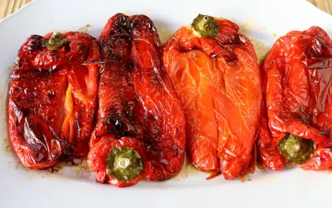 Cuatro pimientos rojos asados en freidora de aire, jugosos y con la piel ligeramente tostada, servidos en una bandeja blanca.