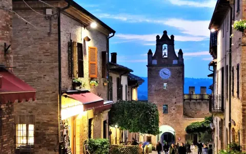 Serata magica al castello di Gradara. Vicoli illuminati, torre dell'orologio e gente che passeggia.