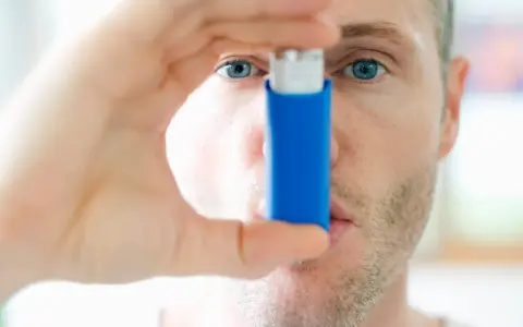 Mann mit blauen Augen hält einen blauen Inhalator, ein reliever asthma.