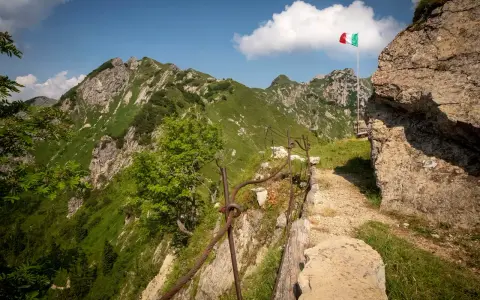 Sentiero della Pace tra montagne verdi, con bandiera italiana che sventola. Un percorso che ricorda la storia.