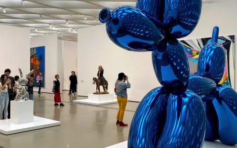 Visitors admire a giant blue balloon dog sculpture in a modern art gallery, a highlight among the top art galleries in the world.