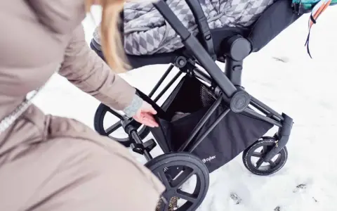 Kobieta wkłada coś do kosza wózka Cybex Priam. Waga wózka jest niewielka, co ułatwia manewrowanie w śniegu.