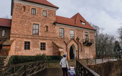 Rodzina idzie drewnianym mostkiem do ceglanego zamku w Oporowie.