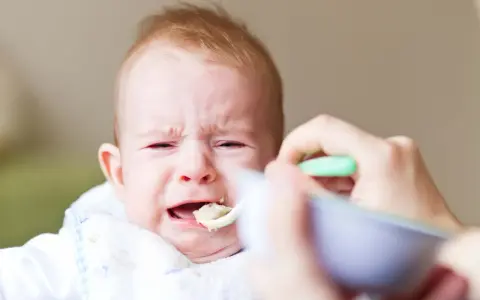 Płacz rocznego dziecka, które nie chce jeść samodzielnie. Mama próbuje nakarmić je łyżeczką.
