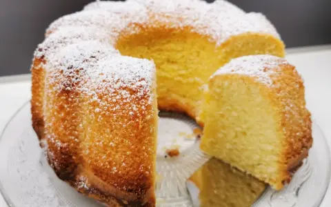 Wilgotna babka z ajerkoniakiem, oprószona cukrem pudrem, prezentuje się apetycznie na szklanej paterze.