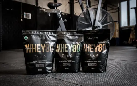 Tre påsar med Wellaware Whey80 proteinpulver står uppradade på ett gymgolv. Perfekt för återhämtning efter träning, oavsett om du föredrar vassle eller kasein.