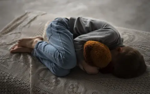 Un niño abraza un peluche, acurrucado en una cama. Una imagen que evoca la necesidad de saber como explicar la muerte a un niño.