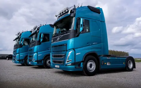 Rząd lśniących, turkusowych ciężarówek Volvo FH gotowych do transportu żywności.