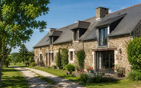 Longère moderne en pierre avec un chemin de gravier menant à l'entrée. Un jardin fleuri borde la façade.