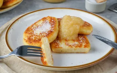Goldbraune Quarkkeulchen, bestreut mit Zucker, serviert mit Apfelmus. Ein leckeres Quarkkeulchen Rezept zum Genießen.
