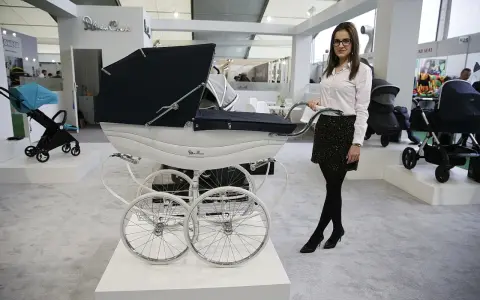 Elegancka kobieta prezentuje najdroższe wózki dziecięce, w tym luksusowy model Silver Cross z białym koszem i czarną gondolą.