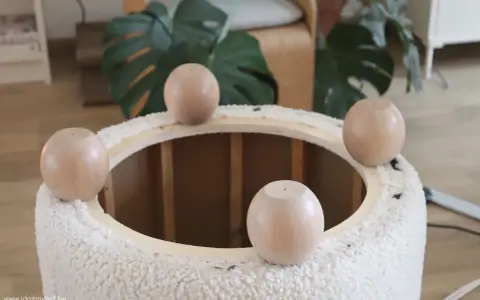 Quatre pieds ronds en bois sont posés sur le bord d'un pouf rond en tissu bouclette, prêt à recouvrir.