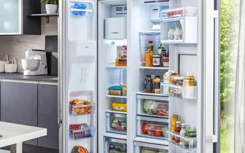 Offener Kühlschrank mit Lebensmitteln, darunter gefrorene Produkte und Getränke. Die Temperatur im Gefrierschrank ist ideal für die Lagerung.