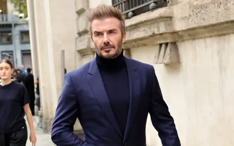 David Beckham luce un elegante traje azul con jersey de cuello alto, caminando con confianza.