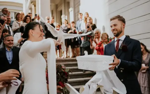 Para młoda wypuszcza gołębie na kameralnym weselu. W tle widać gości z telefonami.