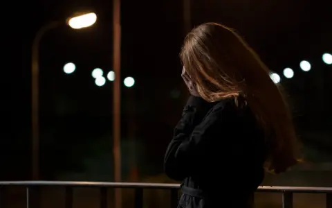 Kobieta z rudymi włosami, zakrywająca twarz dłońmi, stoi na balkonie nocą. W tle migoczą światła uliczne, symbolizujące stres przed seksem.
