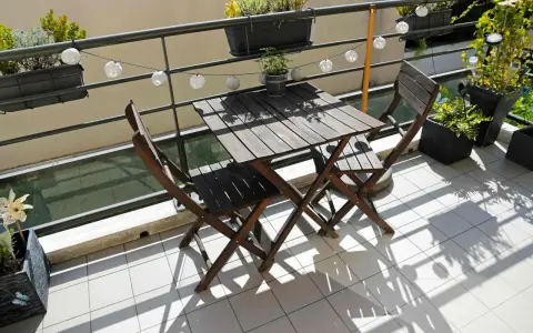 Un piccolo tavolo e sedie in legno su un balcone, con piante e lucine, perfetti per trasformare il balcone in terrazzo.