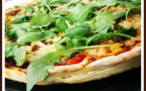 Pyszna pizza z rukolą, pomidorami i serem, pachnąca ziołami. Idealna na szybki obiad.
