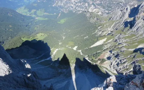 Ombra delle **Torri del Vajolet** che si allunga su un paesaggio alpino di boschi e valli verdi.