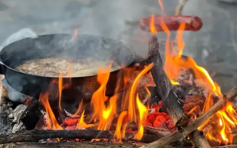 Matlagning över öppen eld, en härlig del av sportlov aktiviteter. Korv och mat i panna över flammande ved.