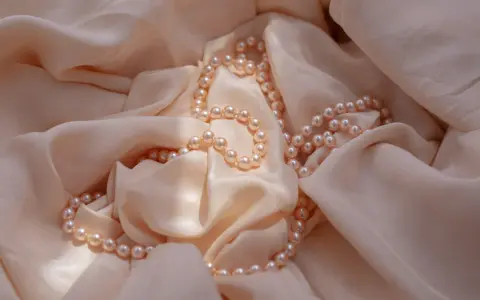 Un filo di perle rosa pallido adagiato su una morbida seta color crema. Un'idea perfetta per regalare perle.