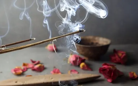 Humo de incienso de lavanda asciende, evocando paz y el significado espiritual de la calma. Pétalos secos y un cuenco completan la escena.