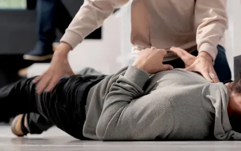 Mann liegt am Boden, Hände versuchen zu helfen. Ein Krampfanfall, aber keine Epilepsie.