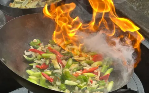 Ogień płonie w woku, przygotowując warzywa do stir fry. To szybkie smażenie, które zachowuje świeżość składników.
