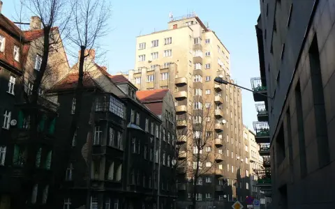 Wysoki, jasny drapacz chmur w Katowicach góruje nad starą kamienicą.