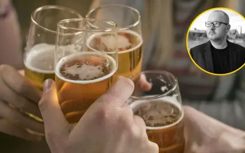 Ludzie wznoszą toasty piwem, podczas gdy w tle widać mężczyznę w okularach, który może symbolizować problem z alkoholem.