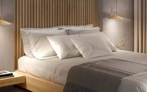 Lit et sa tête de lit en bois, oreillers blancs, lampe dorée. Une ambiance douce pour la deco de chambre.