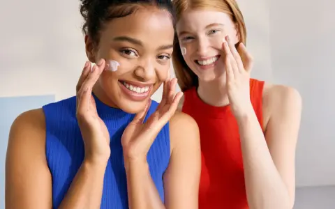 Dos mujeres sonríen mientras aplican crema en sus rostros. Piel con piel hasta cuando, la belleza natural se realza con cuidado.
