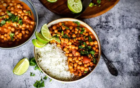 Herzhafte Kichererbsen Rezepte: Ein Teller mit Reis und Kichererbsen-Curry, garniert mit Limettenspalten und Koriander.