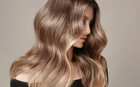 Mujer con cabello largo y ondulado, con un degradado de castaño a rubio. Un ejemplo de cómo aclarar el pelo teñido para un look natural.