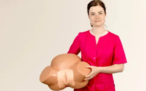 Kobieta w różowej bluzce trzyma model miednicy, demonstrując anatomię do nauki masażu szyjki macicy.