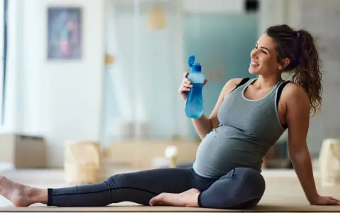 Donna incinta sorride con una bottiglia d'acqua dopo una sessione di yoga in gravidanza.