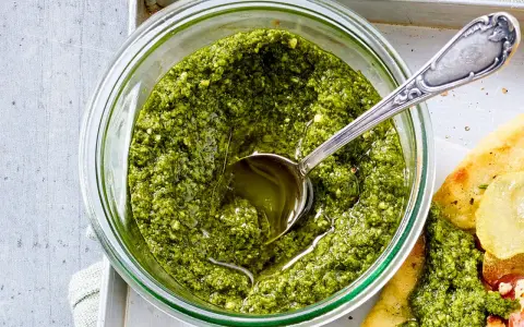 Frisches Basilikum Pesto in einem Glas, mit einem Löffel darin. Perfekt für Pasta oder Bruschetta.